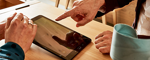 Device Management mit intelligentem IoT Gateway  Finger zeigt auf Tablet-Bildschirm bei Besprechung am Holztisch mit digitalen Inhalten