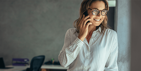Eine Frau steht lächeln am Fenster in einem dunklen Büro und telefoniert