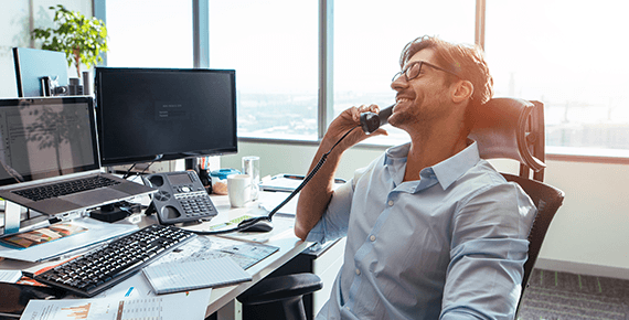Ein Mann sitzt entsannt in einem Schreibtischstuhl und telefoniert mit einem Festnetztelefon