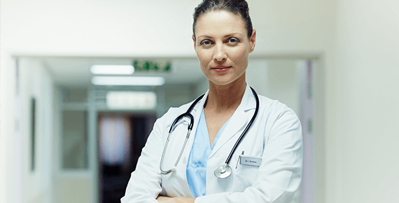 Eine Ärztin mit steht mit weißem Kittel und Stetoskop um den Hals auf einem Gang.