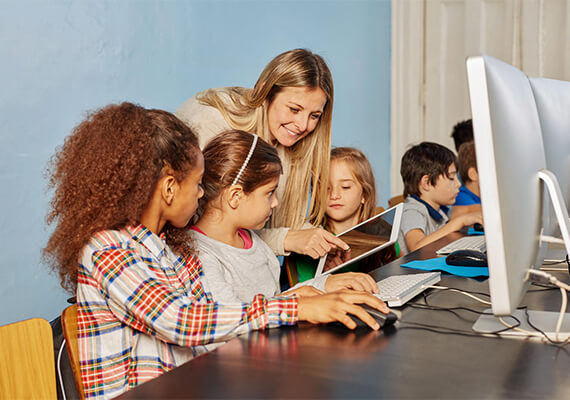 Lehrerin unterstützt Kinder beim Lernen mit Tablet und PC, digitale Bildung in der Grundschule