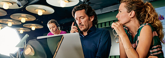 Fokussiertes Teammeeting im Büro Mann telefoniert, Kollegin mit Headset, Team bespricht Projekte am Laptop im modernen Raum