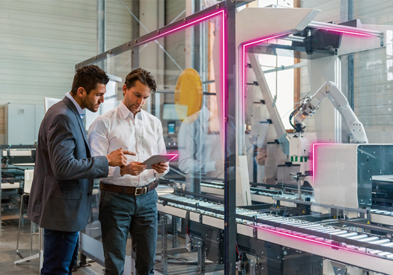 Zwei Implementierungspartner prüfen Roboteranlage, besprechen Daten auf Tablet in moderner Produktionshalle