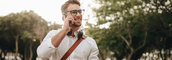 Ein junger Mann mit Brille und weißem Hemd telefoniert während er draußen spazieren geht