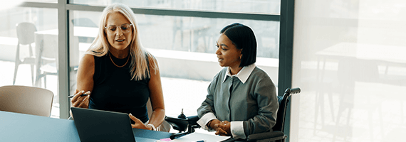 Zwei Frauen sitzen in einem hellen Büro am Tisch und blicken auf einen Laptop
