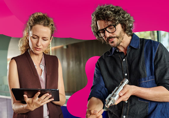 Zwei Personen im Arbeitsumfeld betrachten gemeinsam ein Tablet und ein technisches Bauteil.