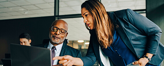 Zwei Kollegen arbeiten gemeinsam im Büro und besprechen ein Problem vor dem Laptop