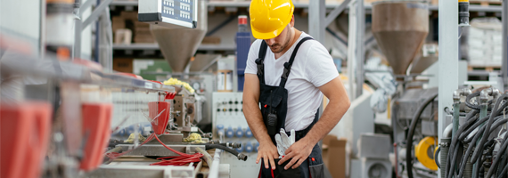 Techniker im Overall prüft Ausrüstung an Fertigungsmaschine in moderner Fabrikumgebung