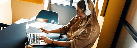 Eine Frau trägt Kopfhörer und lächelt, während sie an einem Laptop arbeitet