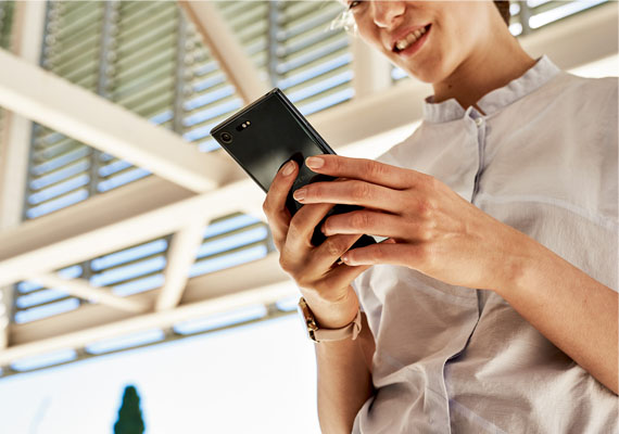 Junge Frau schaut auf Handy in ihren Händen