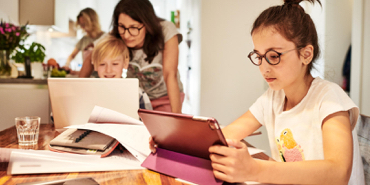 Familie nutzt Tablets und Laptop am Küchentisch