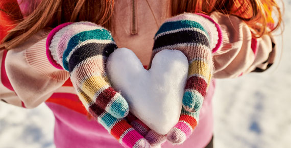 Mädchen hält eine Schneekugel in Herzform in bunten Handschuhen