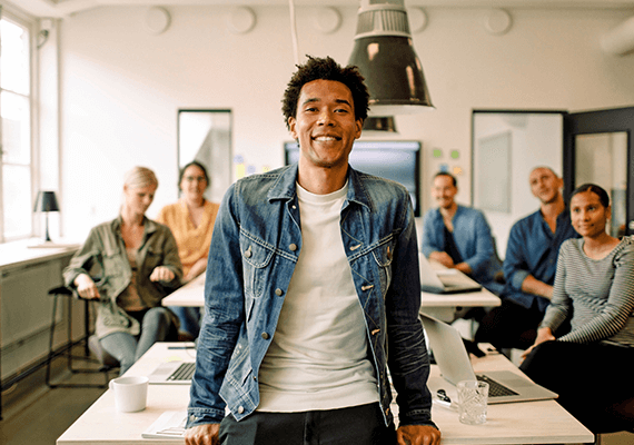 Ein junger Mann steht vor einer Gruppe Menschen im Büro und lächelt