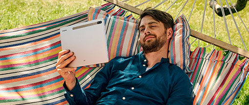 Ein junger Mannmit Tablet  liegt in einer Hängematte.