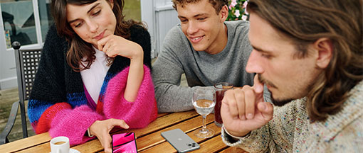 Zwei junge Männer und eine junge Frau sitzen bei Tisch und unterhalten sich Zwei junge Männer und eine junge Frau sitzen bei Tisch und unterhalten sich