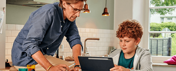 Vater und Sohn nutzen gemeinsam ein Tablet in der Küche Ein Mann und ein Junge sitzen in einer Küche und schauen zusammen auf ein Tablet