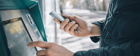 Bankomat Eine Person bedient ein Mobiltelefon, während sie an einem Geldautomaten steht.