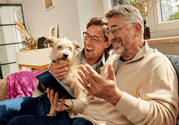 Selbstinstallation Zwei Männer mit Hund nutzen gemeinsam ein Tablet im Wohnzimmer – stabiles WLAN für Streaming und digitales Leben zuhause.