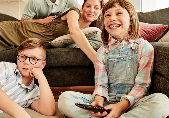 Lachendes Kind mit Fernbedienung vor TV, gemeinsame Familienzeit beim Fernsehen im Wohnzimmer