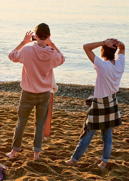 Reisen Zwei Personen stehen barfuß am Strand, eine macht ein Foto vom Meer mit dem Smartphone, die andere genießt den Ausblick mit Händen im Nacken.
