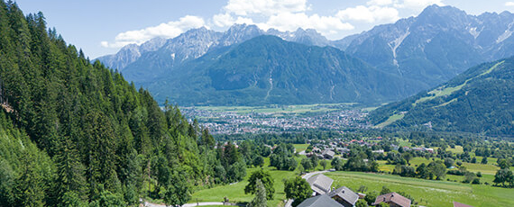 Lienz Weitblick über ein grünes Tal mit verstreuten Häusern, dichten Wäldern und der Stadt Lienz im Hintergrund, umrahmt von hohen Alpenbergen.