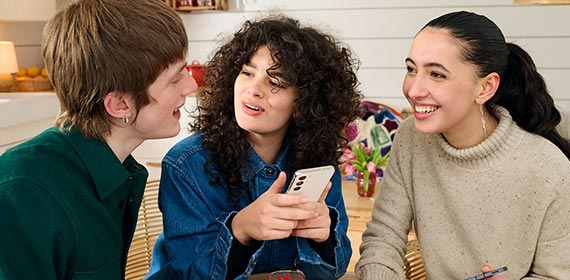Ein junger Mann und zwei junge Frauen mit Mobiltelefon unterhalten sich