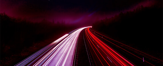 Speedtest Langzeitbelichtung einer Autobahn bei Nacht. Weisse und rote Lichtspuren der fahrenden Fahrzeuge erstrecken sich dynamisch entlang der Strasse.