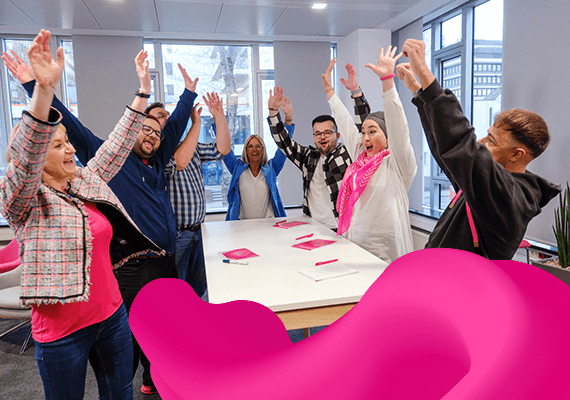 Gruppe fröhlicher Menschen hebt gemeinsam die Arme in einem modernen Büro, wirkt motiviert und feiert einen gemeinsamen Erfolg.