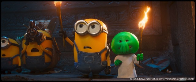 Ein Minion und eine kleine grüne Figur stehen mit Fackeln in einer dunklen Höhle und blicken überrascht nach vorne.