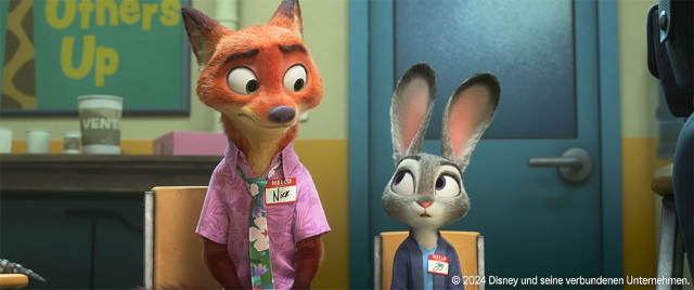 Szene Zoomania Animierte Figuren, ein Fuchs und ein Hase, sitzen nebeneinander auf Stühlen und tragen Namensschilder.