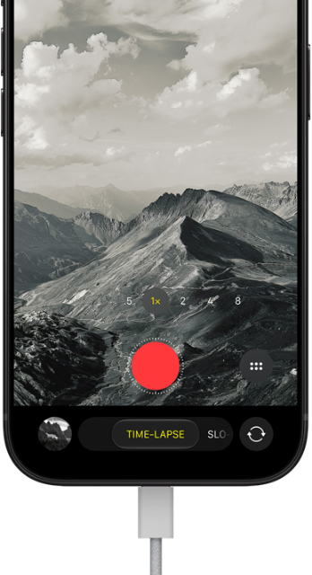 iPhone 18 Pro, Vorderseite, das Display zeigt eine Berglandschaft, mit der Kamera Modus Überlagerung im Zeitraffer Modus, mit dem Netzkabel am Ladeanschluss