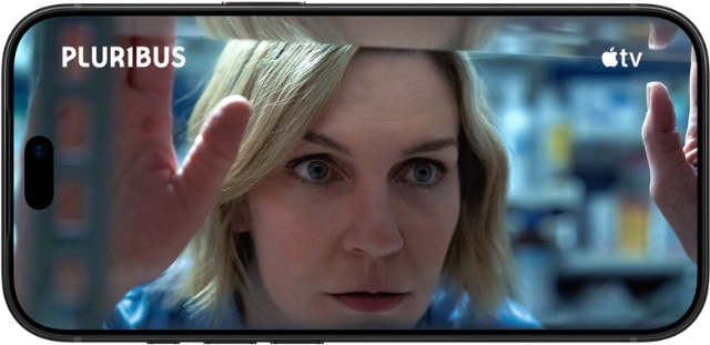 Ein iPhone 18 Pro im Querformat, das Display zeigt eine Nahaufnahme einer Frau, die aus einem Fenster schaut. Serienname: Pluribus