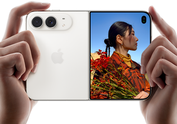 iPhone Duo, Farbe Sternenweiß, in zwei Händen im Querformat gehalten, aufgefaltet, linke Seite mit 48 MP Dual Fusion Rückkameras, rechte Seite zeigt eine Person, die fotografiert wird, auf dem äußeren Display kann die fotografierte Person während der Aufnahme mit Duo Preview ihr Gesicht sehen